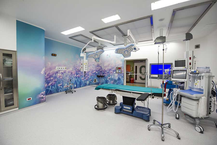 Operating room — sterile, fully equipped, with a softening floral mural on the back wall.