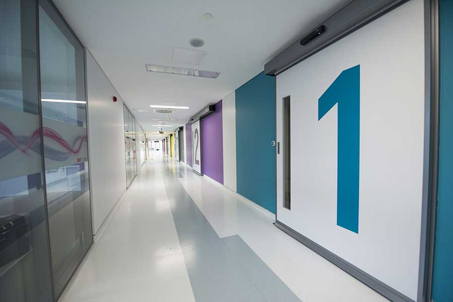Numbered operation-hall corridor — glass partitions, colour-coded wayfinding to each theatre.